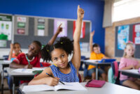 African american girl raising her hands while sitting on her desk in the class at school. school and education concept