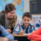 A Caucasian female elementary school teacher helps her student in her classroom.