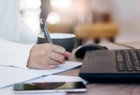 Cropped shot of hand Young female using laptop working at home and writing her plan on paper, Concept work from home
