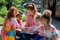 A front view of a teacher and her excited little pupils sitting and doing storytime outdoors in the schoolyard on the benches on a wonderful summer's day in Hexham in the North East of England.